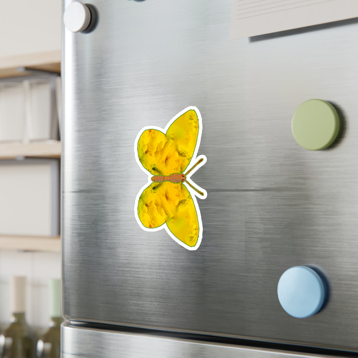 Refrigerator mock-up: butterfly decal showing golden-yellow wings with soft orange mottling and dark green accents near the body, beside green and blue round magnets.