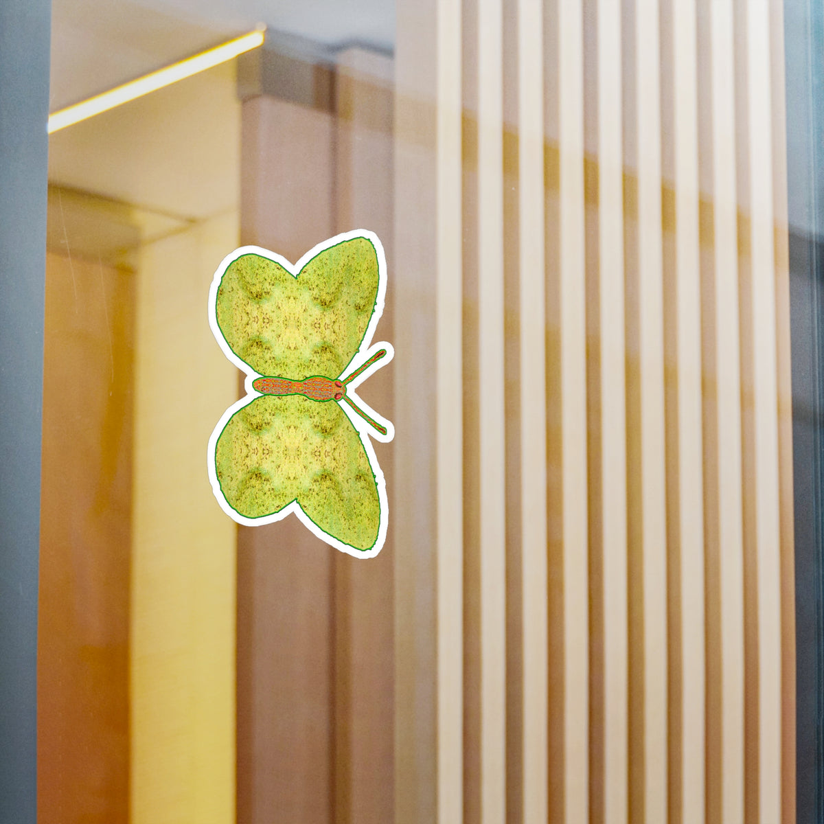 Glass-panel mock-up: white-edged butterfly decal showing pale yellow-green wings patterned with fine olive rosettes, with pale vertical slats behind.