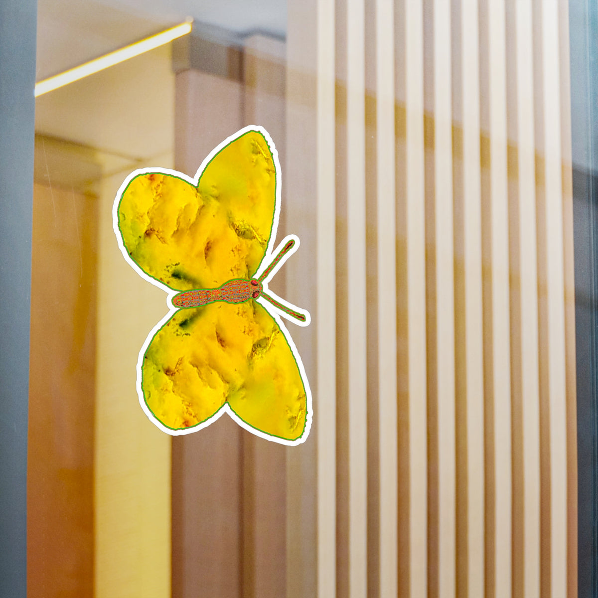 Glass-panel mock-up: white-edged butterfly decal showing golden-yellow wings with soft orange mottling and dark green accents near the body, with pale vertical slats behind.